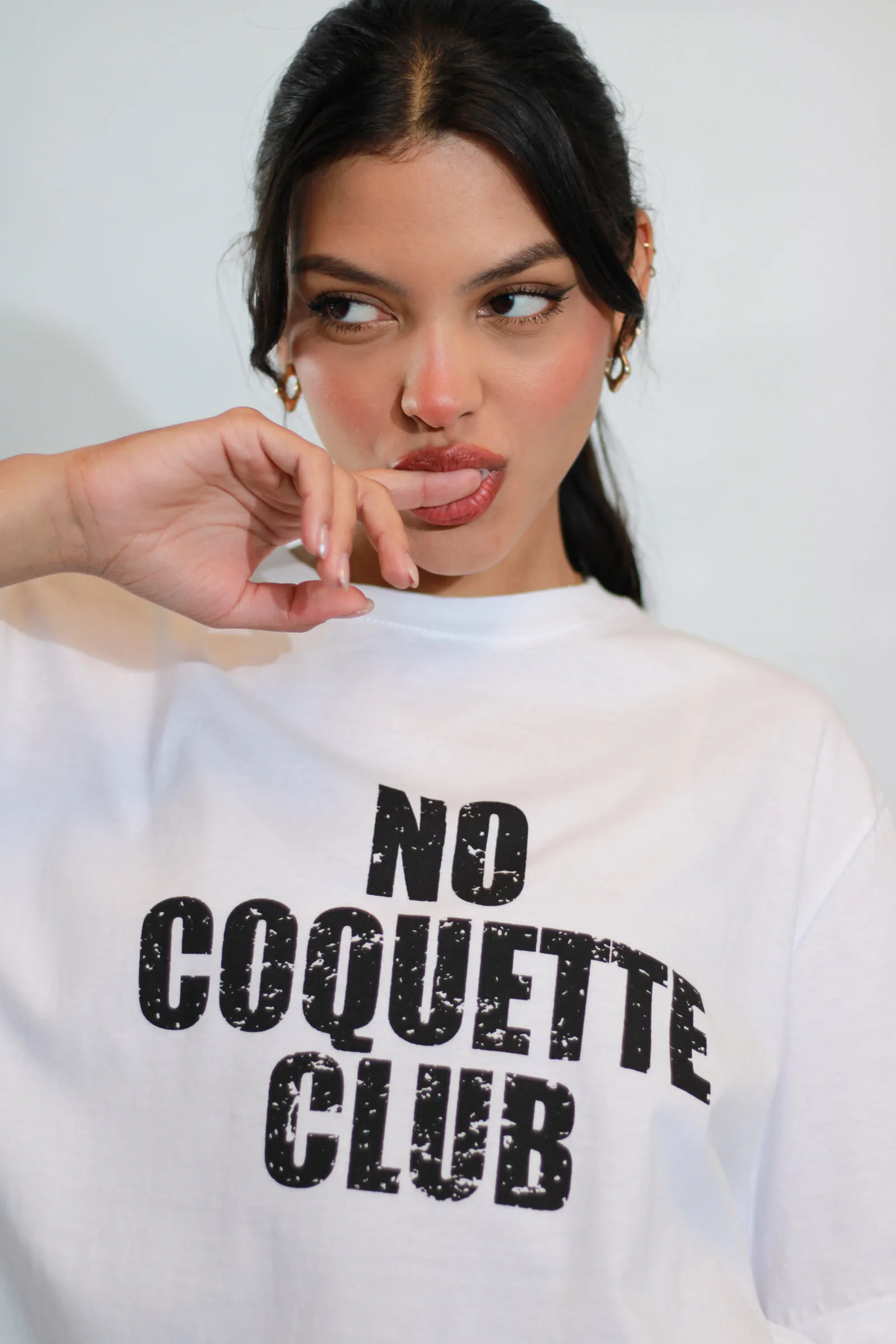 Modelo con remera blanca estampada con la frase «No Coquette Club» sobre fondo claro.